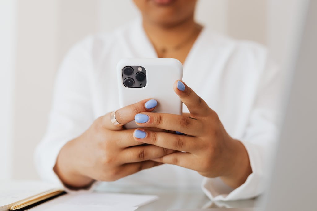 Close-up of a person using a smartphone with pastel nails, showcasing modern technology indoors.